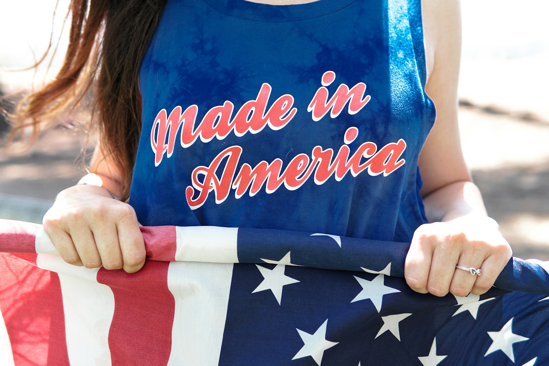 Woman holding an American flag and wearing a blue 'Made in America' tank top in warm sunlight